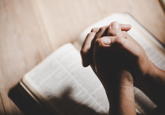 Praying - folded hands over a bible - The Hope Connection