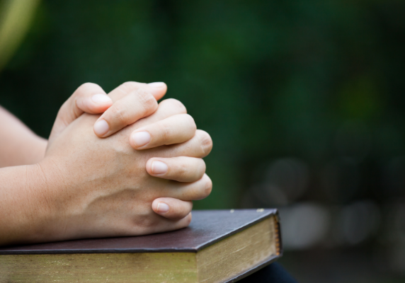 Folded hands on a bible of someone praying - The Hope Connection