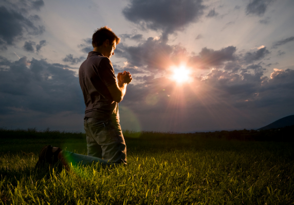 Man praying in a field with sun setting - The Hope Connection